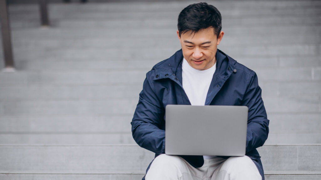 Man working on a laptop while sitting on steps outdoors.