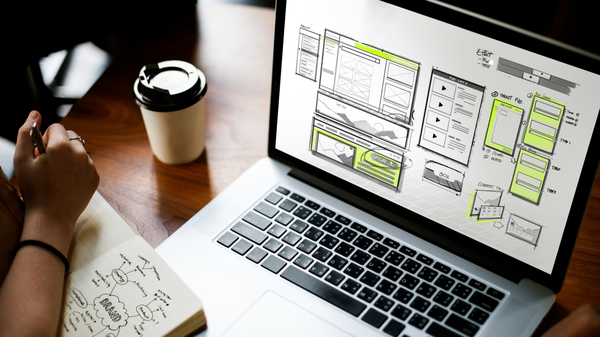 Person planning web design with sketches on laptop in Singapore office setting.