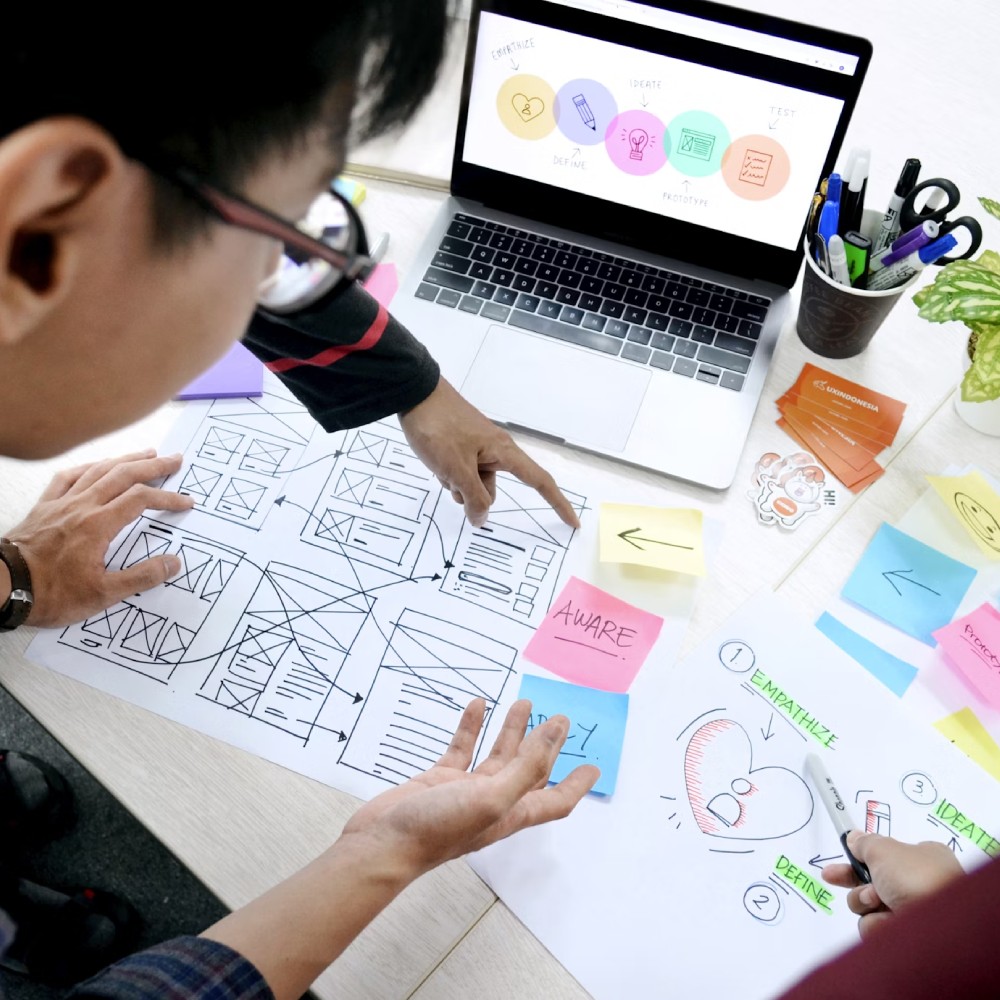 Team brainstorming web design layouts with laptop and colorful sticky notes.